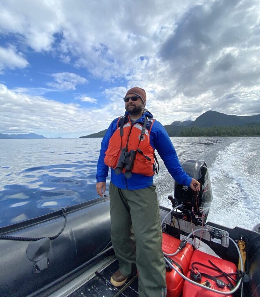 Captain Eric Man drives a Zodiac boat on a calm ocean under bright clouds and a patch of blue sky